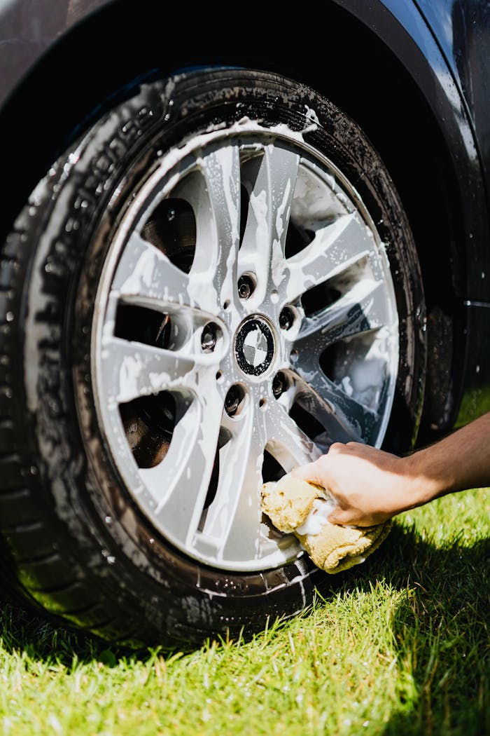 why-choose-us Close-up of a car wheel with soap suds and hand cleaning it on grass.