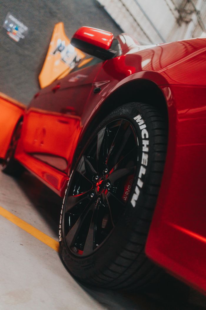 Close-up of a sleek red sports car showcasing a Michelin tire in a garage setting.