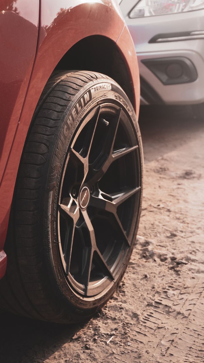 Detailed view of a red car's wheel on a dirt road, showcasing tire tread and custom rim design.