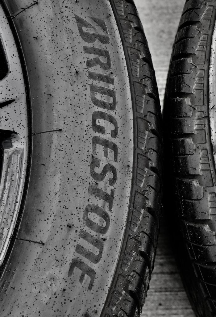 services-img Detailed black and white close-up of wet Bridgestone car tires on asphalt.