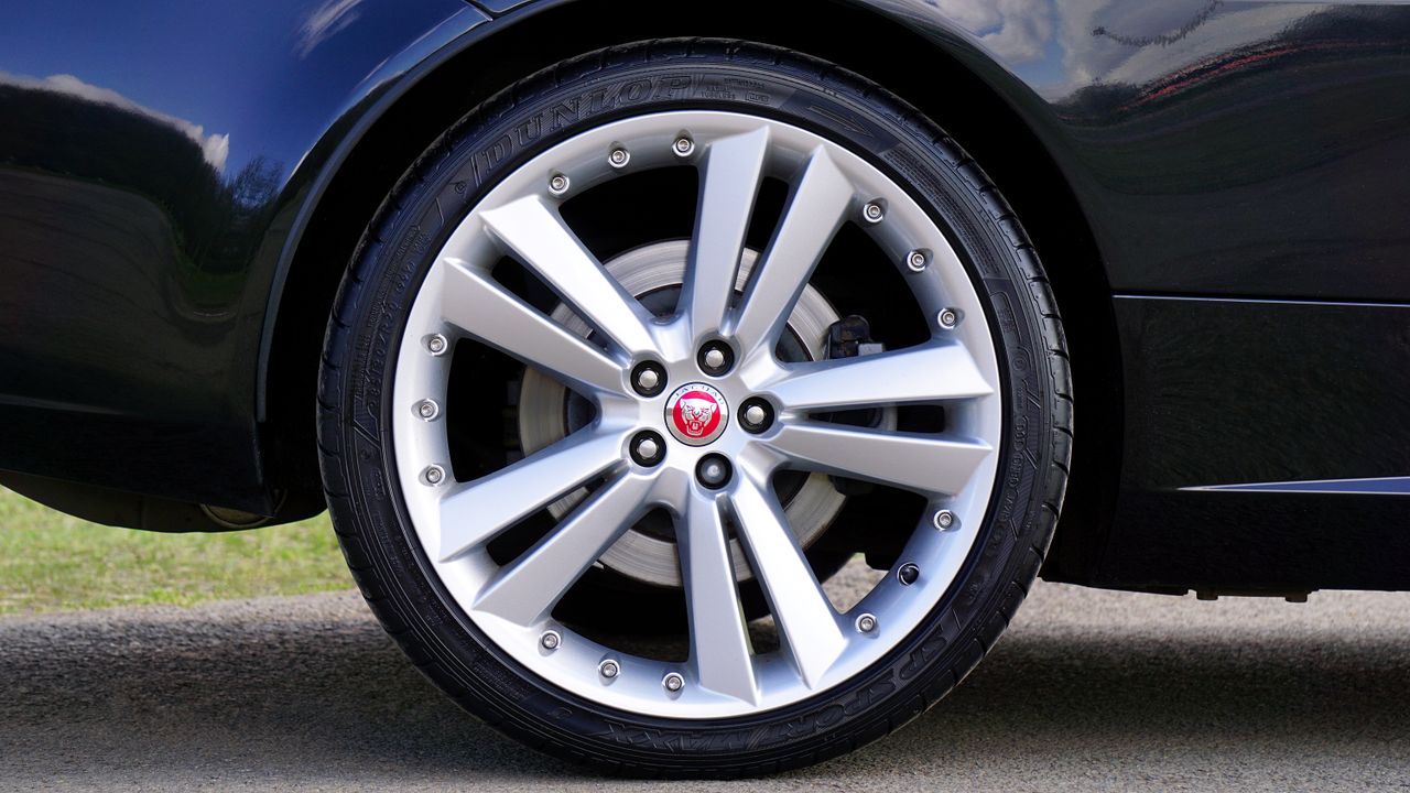 services-01 Detailed image of a shiny Jaguar car wheel with alloy rim, outdoors in the UK.
